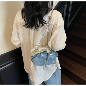 Detail of blue denim pleated bag featuring metallic butterfly charms and silver chain strap