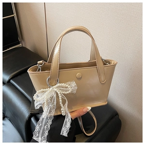 Dettaglio borsa a secchiello beige con ciondolo a fiocco di pizzo e perle e manici