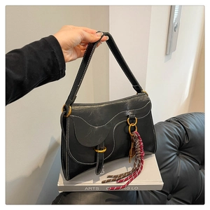Detail of a black leather saddle bag featuring white contrast stitching and gold buckle