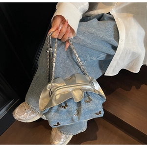 Detail of denim shoulder bag featuring metallic butterfly accents and silver wavy trim