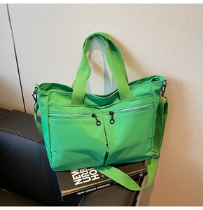 Detailed view of a green nylon tote bag featuring front pockets on a textured surface