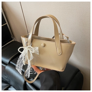 Dettaglio borsa a mano beige in ecopelle con fiocco in pizzo e ciondolo di perle