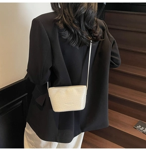 Detail view of a white woven texture crossbody bag on a model wearing a black blazer