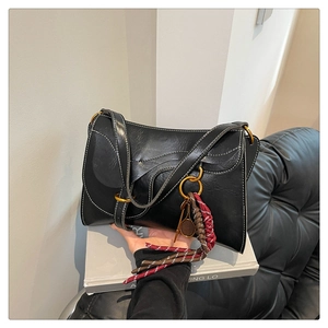 Detail of black crossbody bag with wavy flap, contrast stitching, and tennis tassel charm