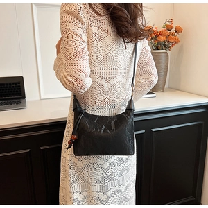 Detail einer schwarzen Umhängetasche mit Perlenanhänger auf weißem Spitzenkleid