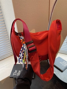 Red crescent nylon crossbody bag with wide adjustable strap and woven pendant