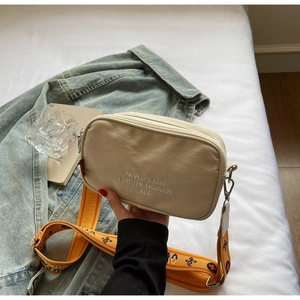 Close-up of beige canvas camera bag with orange jacquard strap and embroidery
