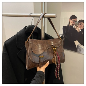 Detail of dark brown leather saddle bag with brass buckle and braided tassel ornament
