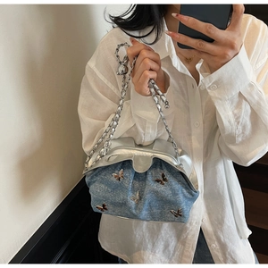 Detail of light blue denim cloud bag featuring silver butterfly charm and chain strap