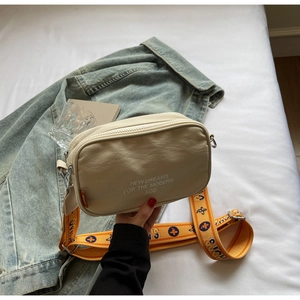 Detail of off-white canvas camera bag with orange jacquard strap and modern print