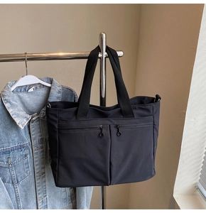 Detail view of black nylon tote bag featuring two front zipper pockets and durable shoulder straps