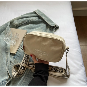 Detail of beige canvas camera bag with New Dreams embroidery and wide woven strap