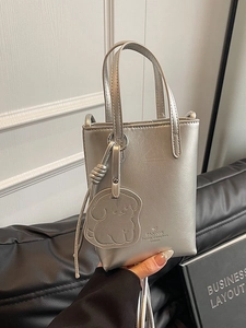 Mini metallic silver bucket handbag with dog charm on black leather background