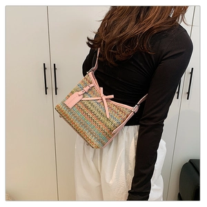 Close-up of woven shoulder bag featuring colorful wavy patterns and pink leather bow detail