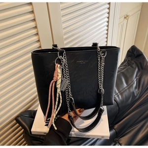 Detail of black leather tote bag with silver chain and woven rope decorative charm