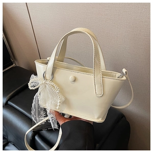 Dettaglio borsa a secchiello bianco panna con elegante fiocco in pizzo e ciondolo di perle