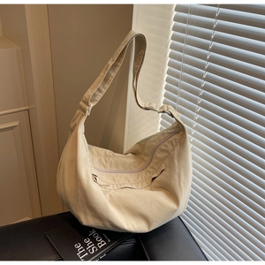 Detail of minimalist beige canvas crescent bag with adjustable strap and front zipper pocket