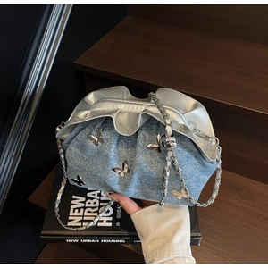 Detail of light blue denim cloud bag with silver metal butterfly accents and chain strap