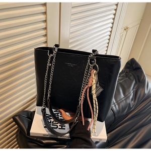 Close-up of black leather tote bag with silver chain strap and colorful woven charms