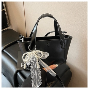 Dettaglio mini borsa nera con fiocco in pizzo bianco e ciondolo di perle sintetiche