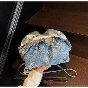 Detail of denim cloud bag featuring 3D silver butterflies and chain strap on stairs