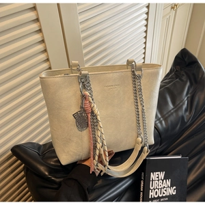 Detail of beige tote bag with silver chain strap and tennis racket charm accessory
