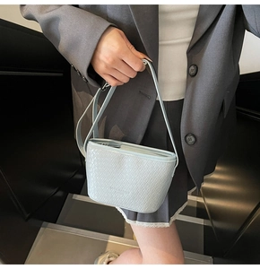 Close-up of woven texture and brand logo on light grey-blue faux leather bucket bag