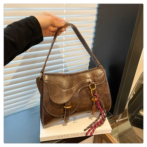 Detail of vintage dark brown leather saddle bag with woven tassel and metal key charm