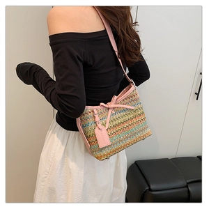 Close-up of bohemian colorful woven straw bag with pink leather bow and shoulder strap detail
