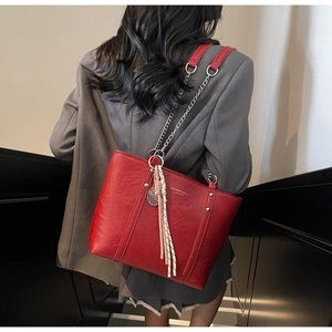 Detail of red pebbled leather tote bag with silver chain strap and woven tassel charm