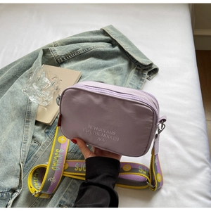 Detail of purple nylon camera bag with white embroidery and colorful floral jacquard strap
