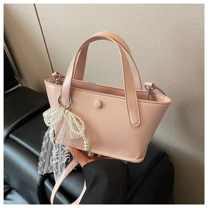 Dettaglio borsa in pelle verniciata rosa con fiocco di perle e ciondolo in pizzo
