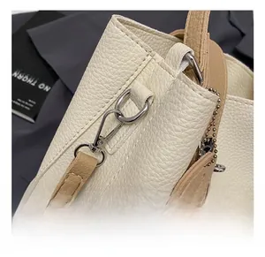 Detail of silver metal lobster clasp and textured lychee leather on cream bucket bag