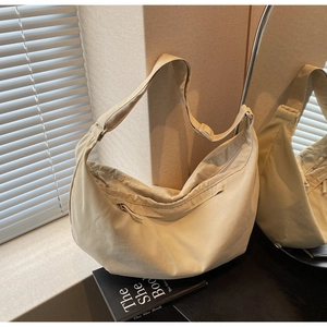 Close-up of minimalist beige nylon crescent bag featuring a smooth zipper and wide strap