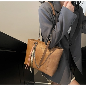 Brown leather tote bag featuring silver chain straps and decorative woven rope charm
