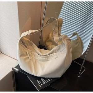 Detail of cream nylon hobo bag with zipper pocket and adjustable strap on a reflective surface