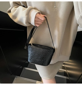 Close-up of black woven leather texture and embossed brand logo on the shoulder bag