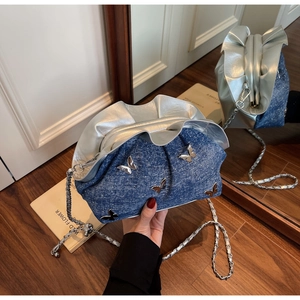 Detail of blue denim shoulder bag featuring silver butterfly charms and chain strap