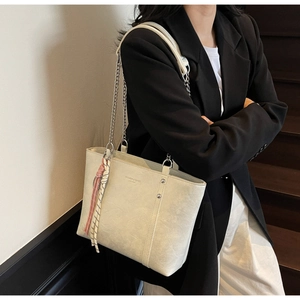 Detail of off-white leather tote bag with metal chain strap and decorative charm