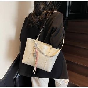 Detail of cream leather tote bag featuring a metal chain strap and colorful silk scarf charm