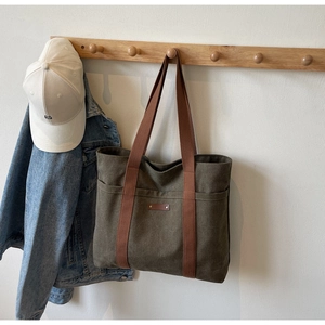 Détail du sac fourre-tout en toile avec écusson en cuir, corps vert olive et anses brunes