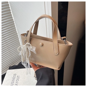 Dettaglio borsa a secchiello in pelle PU beige con ciondolo a fiocco di pizzo e perle
