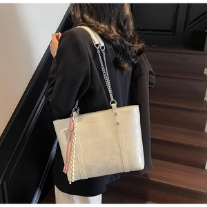 Detail of cream leather tote bag with silver chain strap and stylish tassel on stairs