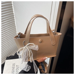Dettaglio borsa a secchiello beige minimalista con ciondolo a fiocco di perle