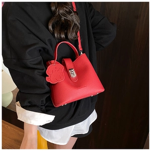 Detail of red lychee leather handbag with metal turn-lock and cute dog charm accent