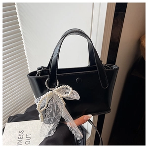 Dettaglio di una borsa a secchiello in pelle PU nera con ciondolo a fiocco e pizzo perlato