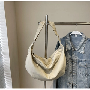 Detail view of beige canvas crescent bag hanging with denim jacket on steel rack