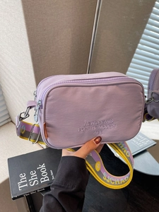 Purple nylon camera crossbody bag with embroidered text and colorful striped strap