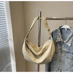 Detail view of cream-white crescent shoulder bag with wide adjustable strap and metal buckle