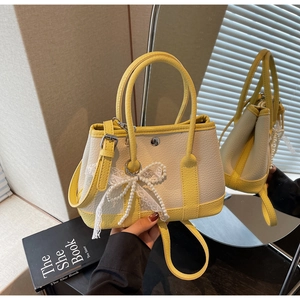 Detail of cream and yellow bucket bag with lychee texture and pearl lace bow charm